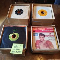 Four cardboard boxes containing approximately 200 records. Visible labels include Apple, RCA Victor, and an Elvis Presley record cover.