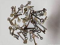 Top view of approximately 50 metal skeleton keys of various sizes and designs scattered on white surface showing details of bow and bit shapes.
