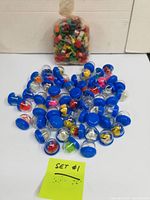 Photo of multiple clear plastic vending machine capsules with blue lids containing small toys, arranged spread out on a flat surface with a tag reading 'SET #1'