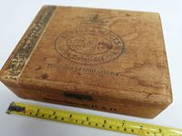 Side view of wooden cigar box with measuring tape showing approximate length of 9 inches and original label tape.