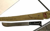 Photo of vintage machete alongside canvas military sheath, showing entire length and sheath markings.