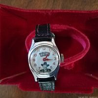 Front view of watch face showing Hopalong Cassidy image and dial with original black leather strap on red velvet cushion.