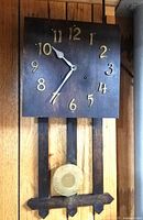 Front view of the vintage wooden wall clock with gold numerals and brass pendulum.