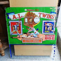 Front side of the Williams 1963 A.L. Twins arcade back glass showing colorful baseball-themed artwork with cutouts for score and inning indicators. Shows some wear and areas of paint chipping.