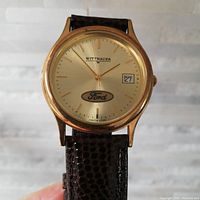 Close-up of the gold-tone Wittnauer watch dial showing the Ford logo and date window.