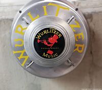 Front view of the Wurlitzer speaker showing the red trumpet player logo and yellow 'WURLITZER' text on the metal cap.