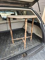 Table standing in vehicle cargo area showing three turned legs and rectangular top
