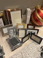 Image of eleven assorted 5x7 photo frames in various styles and materials placed on floor next to a large decorative Christmas ornament.