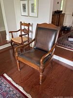 Front perspective of leather upholstered arm chair in wood frame with brass nailhead trim