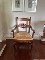 Front view showing carved backrest, arms and woven rush seat