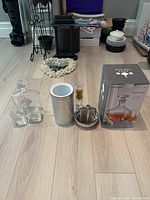 Whiskey decanter set with two glasses and whiskey decanter set in box, silver wine chiller, metal flask with shot glass, all on hardwood floor.