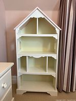 Front view of white house-shaped bookcase with pink roof and multiple compartments