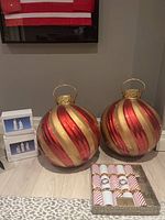 Two large outdoor ornaments with red and gold stripes, two boxed sets of white ceramic nativity figures, and a box of nine Christmas crackers on floor.