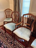 Three dining chairs including one arm chair with light blue upholstered seat and walnut wood frames, arranged in corner of room on rug.