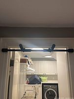 Pull up bar installed horizontally across a white door frame in a room with laundry appliances in background.