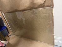 Clear new glass desk top partially wrapped in protective paper in a storage setting.