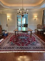 Rectangular hand-knotted wool rug placed under dining table in room, red field with floral medallion and navy border, white fringes