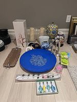 Photo shows an assortment of home decor items arranged on the floor including vases, plates, candle holders, and figurines.