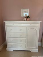 Front view of white painted wood storage chest showing two top drawers, four lower drawers, and side cabinet.