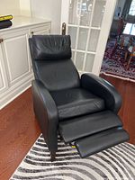 Black leather recliner chair viewed from the front showing the extended footrest and cushioned backrest and armrests.