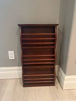Front view of empty wooden magazine rack showing angled shelves and vertical wood grain back panel