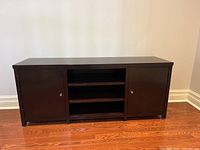 Front closed view of the solid wood media unit with two cabinet doors and central open shelves.