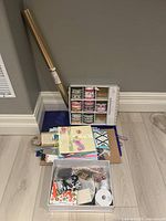 Image of assorted gift wrap supplies including roll of wrapping paper, ribbon spools in rack, assorted gift bags, tags, and other wrapping accessories scattered on floor.