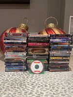 Photo showing multiple stacks of assorted movie DVDs arranged in front of decorative red and gold ornaments on a gray patterned surface.