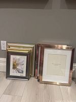 Photo showing six 8x10 photo frames arranged on floor, including three frames with a rose gold metallic finish and inner mat labeled Pottery Barn, two metallic finish frames in gold and silver, and one dark gray frame with flower placeholder image.