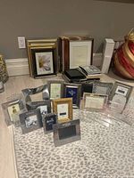 Photo showing 21 assorted photo frames of various designs and sizes, mostly 4x6 and smaller, arranged on a leopard print surface against a grey wall.