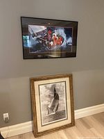 Photo showing both framed sailing photographs, one black framed color image on the wall and the other large gold framed black and white image leaning against wall.