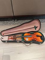 Full shot of the Cremona Junior violin in its hard case with bow, showing the violin's sunburst finish and case interior lining.