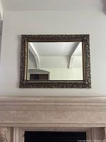 Rectangular wall mirror hung above fireplace showing ornate carved frame and clear reflective surface.