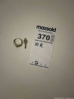 Overhead view showing 10K gold ring and small key-shaped pendant next to auction tag