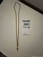 Full length image of gold filled cross pendant on chain necklace laid flat on a surface