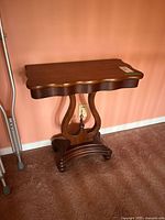 Front side view of the American Empire style hall table showing the scalloped top and lyre-style base with gold painted detail.