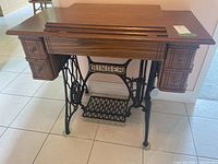 Full view of antique Singer sewing table showing wood finish, four small drawers, and metal treadle base with Singer branding.