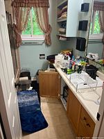 Overall view of bathroom with blue rugs, towels, bathroom supplies on countertop, cabinets, and trash bins.