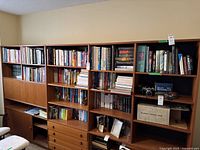 Wide view of wooden wall unit filled with hardcover and paperback books of varied sizes and colors.