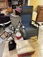 Overview of the camping lot showing the folding camp chair, sun lounger, coolers, and grill basket