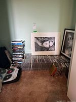 Stacked CDs and concert DVDs alongside framed photos of musicians on the floor.