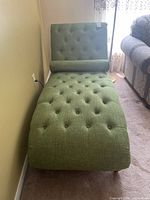 Full view of green upholstered tufted chaise lounge with matching bolster pillow placed against the wall.