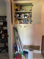 Cleaning supplies including Swiffer mops, brooms, dustpan, and items in cabinet such as garbage bags and household items.