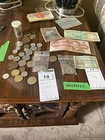 Wide angle photo showing laminated Canadian $2 bill, various other paper currencies, and multiple coins on a wooden table.
