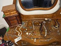 Two wood jewelry boxes on a wooden dresser with various necklaces and jewelry spread out.