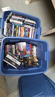Two large blue plastic bins filled with various DVDs, including TV series box sets and movies.