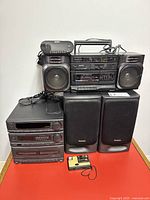 Photo showing entire lot including Technics mini stereo system components stacked, Technics speakers in front, Sanyo boombox on top, Sony click radio on boombox, and Kodak Disc 3100 camera in front bottom.