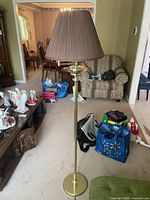 Full view of the floor lamp in a living room setting showing brass base, tall pole, and brown pleated fabric shade.