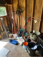 Photo showing various rakes, garden tools, hose and buckets inside a shed.