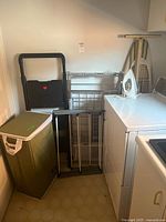 Overview photo showing all items: ironing board, iron, drying racks, step ladder, and laundry basket corner in a laundry room.